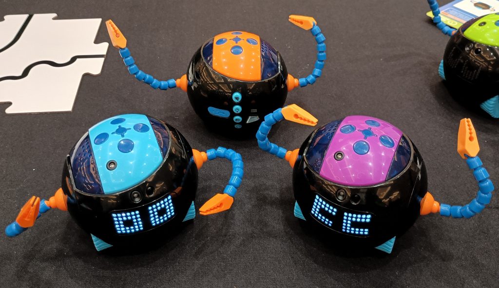 Set of Cooper coding robots in blue, orange, and pink, with lit up LED eyes and a 4th green Cooper at edge of frame.